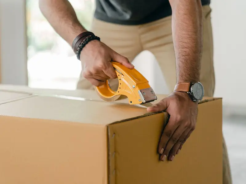 Hands sealing a cardboard box with a packing tape dispenser.