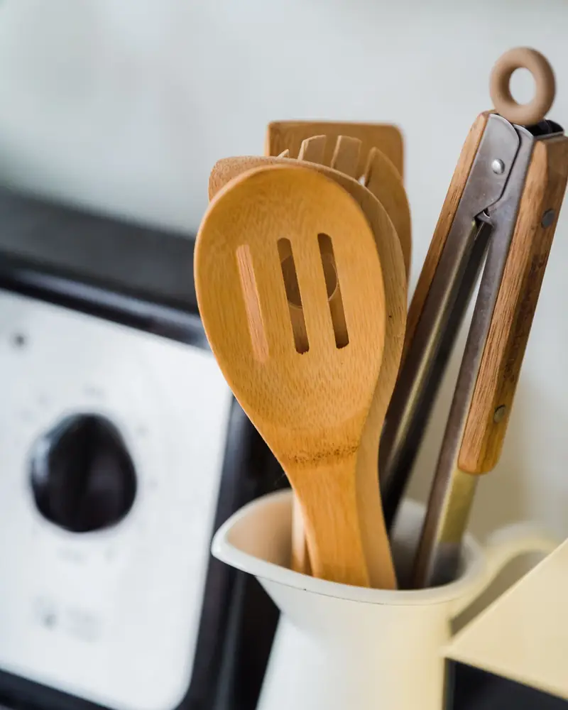 Wooden and metal kitchen utensils standing in a white countertop jug.
